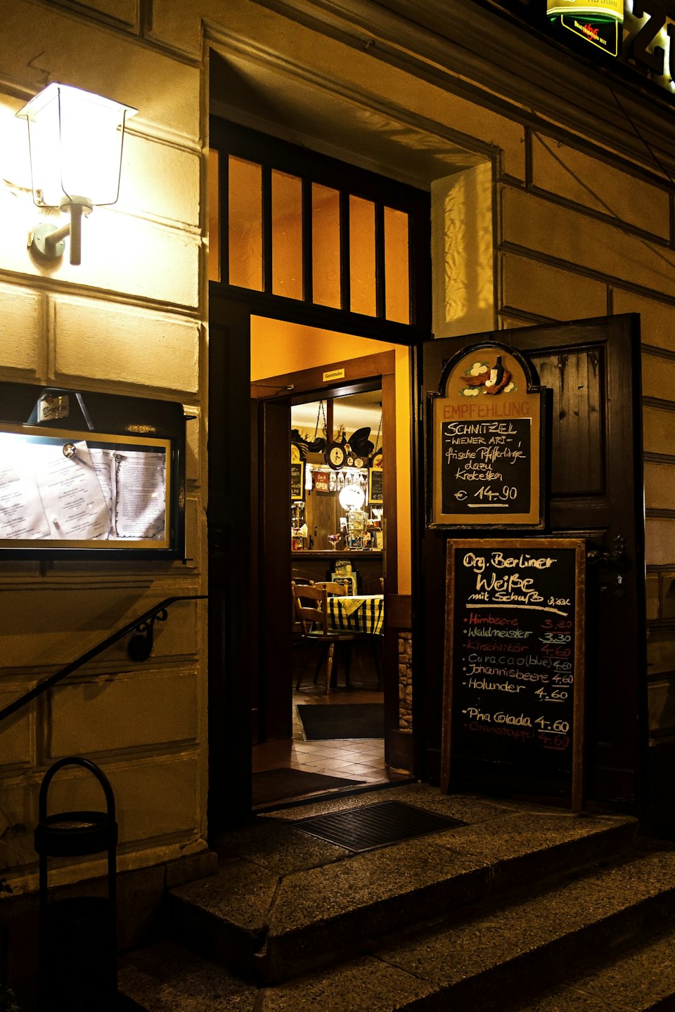 Restaurant-Eingang bei Nacht mit leuchtenden Fenstern und Tafelmenüs.